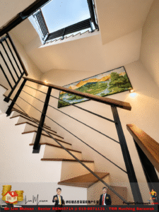 A modern stairwell viewed from below with a skylight above, black metal railing and wooden handrail, and a large landscape painting on the wall.