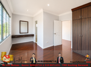 Bright, empty bedroom with dark wood floors, a wall-mounted desk with drawers and a matching framed mirror, large window on the left, and a tall dark wood wardrobe on the right; open door to a hallway.