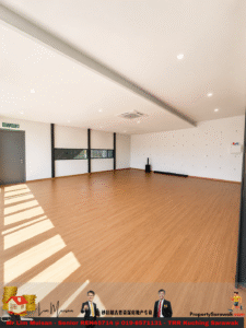 Empty, well-lit multipurpose room with wooden floor, white walls, and large windows letting in sunlight; door labeled 'KELUAR' on left and a few props along the back wall.