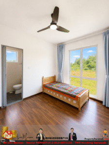 A small bedroom with a wooden single bed, colorful quilt, and large windows overlooking a green field; light blue curtains frame the window.