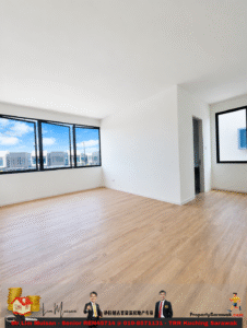 Bright, empty living room with white walls, large windows showing an urban scene, and light wood flooring.