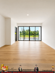 Bright, empty living room with light wood flooring, white walls, and recessed ceiling lights, featuring large floor-to-ceiling glass sliding doors opening to a balcony with a green outdoor view.