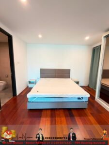Modern bedroom with a queen bed and padded headboard, two small nightstands, and dark wood flooring; bathroom to the left and sliding glass door with curtains to the right.