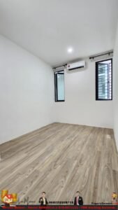 Empty white room with wood-look flooring, two tall windows, and a wall-mounted air conditioner under the ceiling light