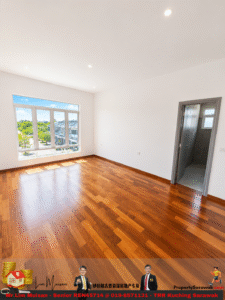 Bright empty room with warm hardwood floors, white walls, and a large window showing a neighborhood view; doorway to a tiled bathroom on the right.