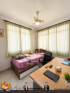 Small bedroom with a pink cartoon-themed bed, a black office chair, and a wooden desk under two large windows with green patterned curtains; ceiling fan overhead and a few pillows and blankets on the bed.