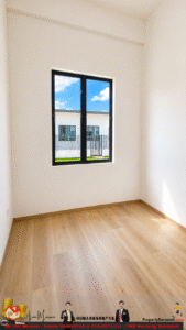 Empty white room with a large black-framed window, light wooden floor, and bright outdoor view of a building and blue sky.