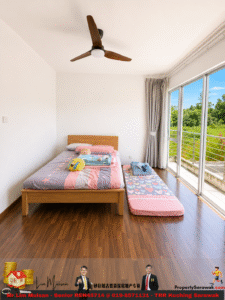 Bright bedroom with a wooden bed and a pink-striped bedspread, two pillows, and a mascot stuffed toy on the bed; a matching floor mattress lies beside it by large windows. Outside view shows greenery.