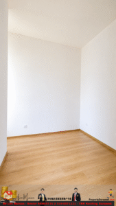 Empty room corner with white walls, wooden floor, baseboards, and two electrical outlets on the walls.