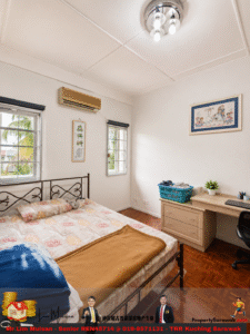 Bright bedroom with a metal-framed bed, patterned sheets, and a brown blanket, two windows with blinds, a wall air conditioner, and wall art above a dresser and desk with a laundry basket on top.