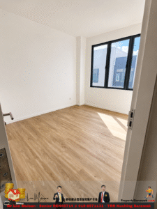 Empty modern room with white walls, light wood flooring, and a large corner window letting in sunlight.