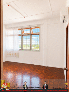 Bright empty room with white walls, polished wooden floor, and a large grid window letting in daylight with sheer curtains on the left.
