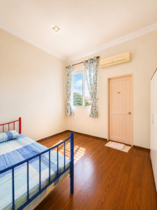 Bedroom with blue metal bed, pastel linens, wooden floor, window with patterned curtains, pink closet door, and AC above the door.