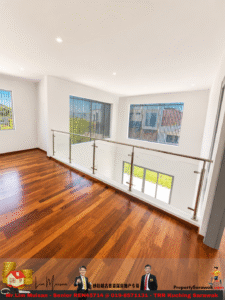Bright open landing with dark wood floors and a glass railing overlooking a two-story foyer with large windows and vertical blinds.