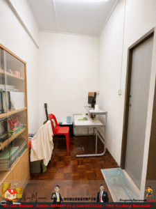 Small home office with a white wall, a metal desk, red plastic chair, a guitar in the corner, and a glass-front cabinet on the left.