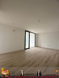 Empty modern living room with light wood flooring, white walls, and a large glass sliding door opening to a balcony; ceiling lights installed but exposed wiring on the floor suggests ongoing renovation.