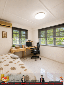Small bedroom home office with a desk, computer, and ergonomic chair by two windows; bed is on the left and a wall-mounted AC above.
