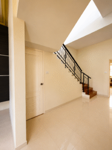 Interior hallway with a closed white door and a wooden staircase with black wrought-iron railing rising to the right, in a beige-toned home interior.