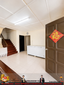 Bright interior hallway with tiled floor, brown door on the right bearing a red 福 decoration, and a white freezer against the back wall; wooden stairs to the left.