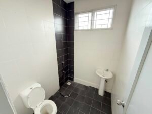 Small bathroom with a white toilet, pedestal sink, and handheld shower hose on black-tiled wall, window above.