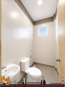 Small beige-tiled bathroom with a white toilet and sink, a small window high on the wall, a wooden door, and a floor drain.