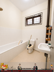 Small tiled bathroom with a white bathtub, toilet, and wall-mounted sink; a barred window above and cleaning tools nearby.