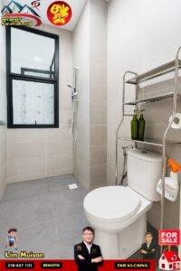 Modern bathroom with gray tiles, white toilet, wall-mounted handheld shower, tall chrome rack, two green bottles, spray bottle, and a frosted window.