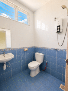 Bright bathroom with white upper tiles and blue tiled lower walls, showing a toilet, wall-mounted sink, and an electric shower unit by the windowed wall at the top left.