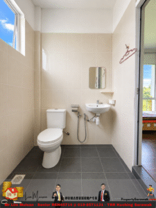 Small beige-tiled bathroom with a white toilet and wall-mounted sink, a small mirror, and a window to the left. Door opens to a bedroom area nearby.