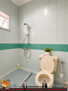 Beige toilet in a tiled bathroom with a green accent stripe, a wall-mounted shower, window, and a potted plant on the tank.