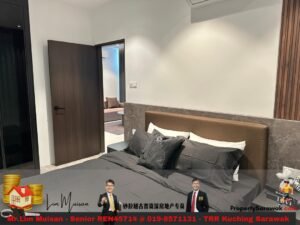 Modern hotel bedroom with a brown upholstered headboard, gray bedding, and an open doorway to a living area.