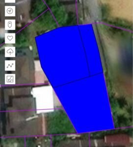 Satellite map showing a blue highlighted land parcel with purple boundary lines. A multi-sided polygon sits over rooftops and open ground.