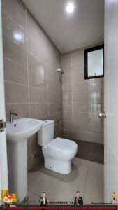 Small beige-tiled bathroom with a pedestal sink, toilet, and a shower area; a frosted window near the ceiling and a recessed light.